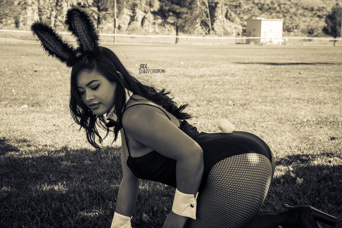 Woman dressed as a bunny with bunny ears, fishnet stockings, crouching on the grass in an outdoor area.