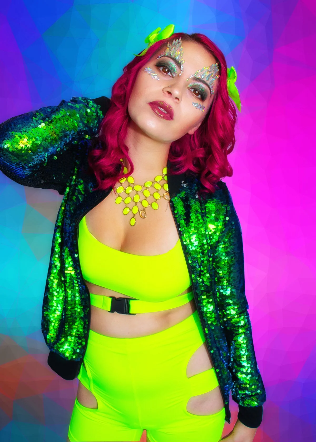 Woman with vibrant pink hair, elaborate makeup with rhinestones on her face, wearing a neon yellow top and pants with cutouts, a black sequined jacket, and a statement yellow necklace, against a colorful abstract background.