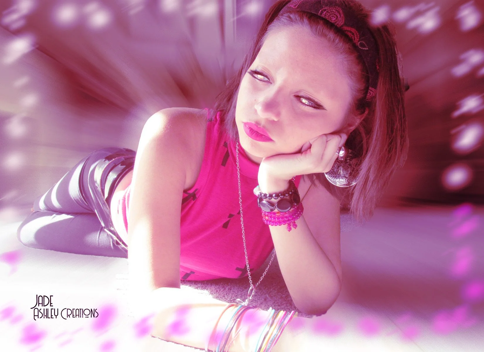 A young woman with short brown hair, wearing a pink sleeveless top, is lying on her stomach with her chin resting on her hand. She is surrounded by pink and purple light effects.