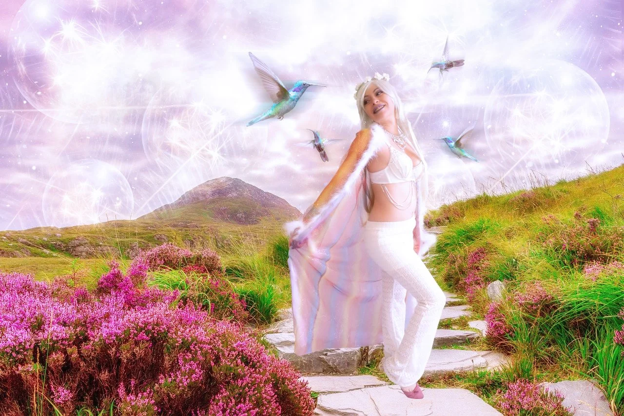 A woman dressed in white standing on a stone pathway in a colorful meadow with pink flowers. She is surrounded by hummingbirds and has a fantasy background with glowing orbs and a glittery sky.
