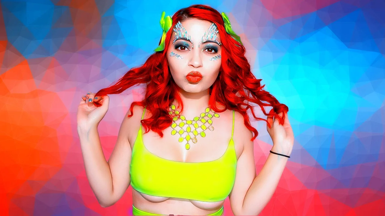 Woman with bright red curly hair, colorful makeup, and neon yellow top, posing against a vibrant abstract background.
