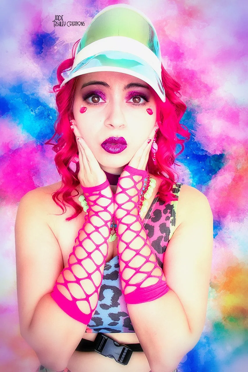 Young woman with bright pink hair, wearing a colorful cap, leopard print top, fishnet arm warmers, and bold makeup, against a vibrant rainbow-colored background.