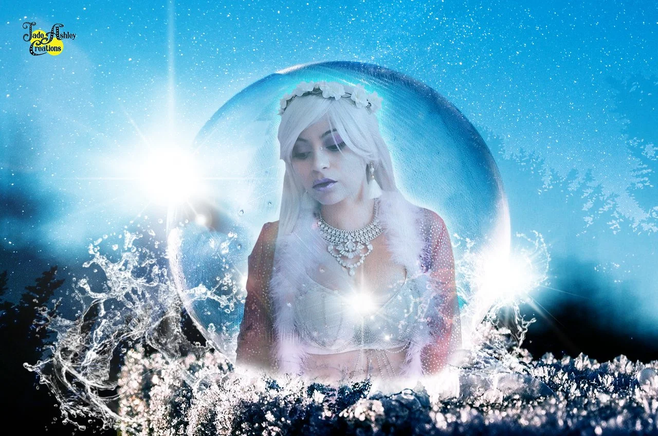 A woman with platinum blonde hair, dressed in white, wearing a flower crown and jewelry, appears inside a transparent ice sphere amid a blue icy landscape with splashing water and bright lights.