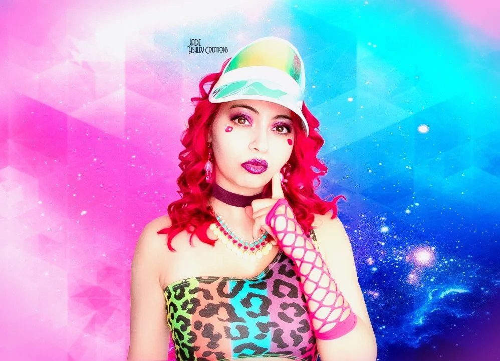 Woman with bright red curly hair in colorful leopard print top, wearing a holographic cap, pink fishnet glove, makeup with bold lipstick and face jewels, posing with a finger on her lips against a vibrant galaxy background.