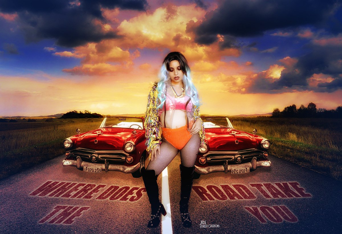 A woman with long hair dyed blue and black standing in front of two red vintage cars on an empty road during sunset. The sky has dramatic clouds in shades of orange, pink, and purple. The words 'WHERE DOES THE ROAD TAKE YOU' are painted on the road s