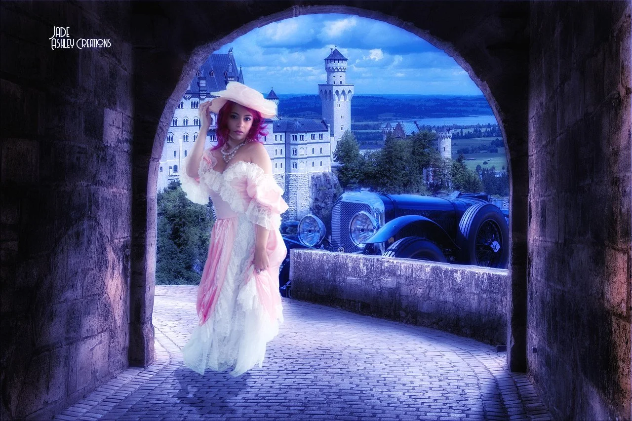 A woman in a Victorian-style dress and large hat standing under a stone archway with a castle and an old-fashioned car in the background.