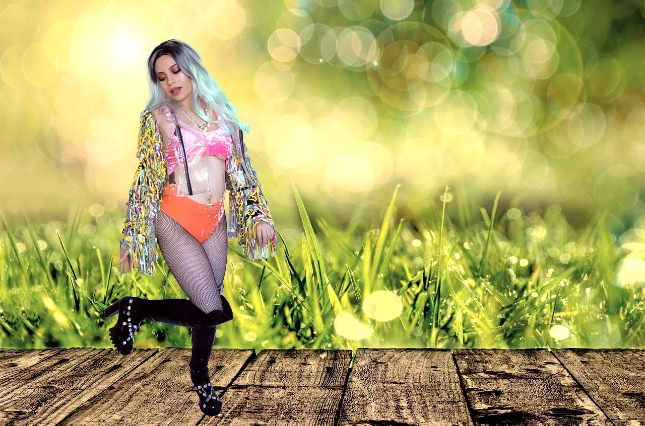 A woman with multicolored hair, wearing a shiny, multicolored jacket, pink crop top, orange shorts, fishnet stockings, and black thigh-high boots, standing on a wooden surface with a bright, bokeh-filled green and yellow background.