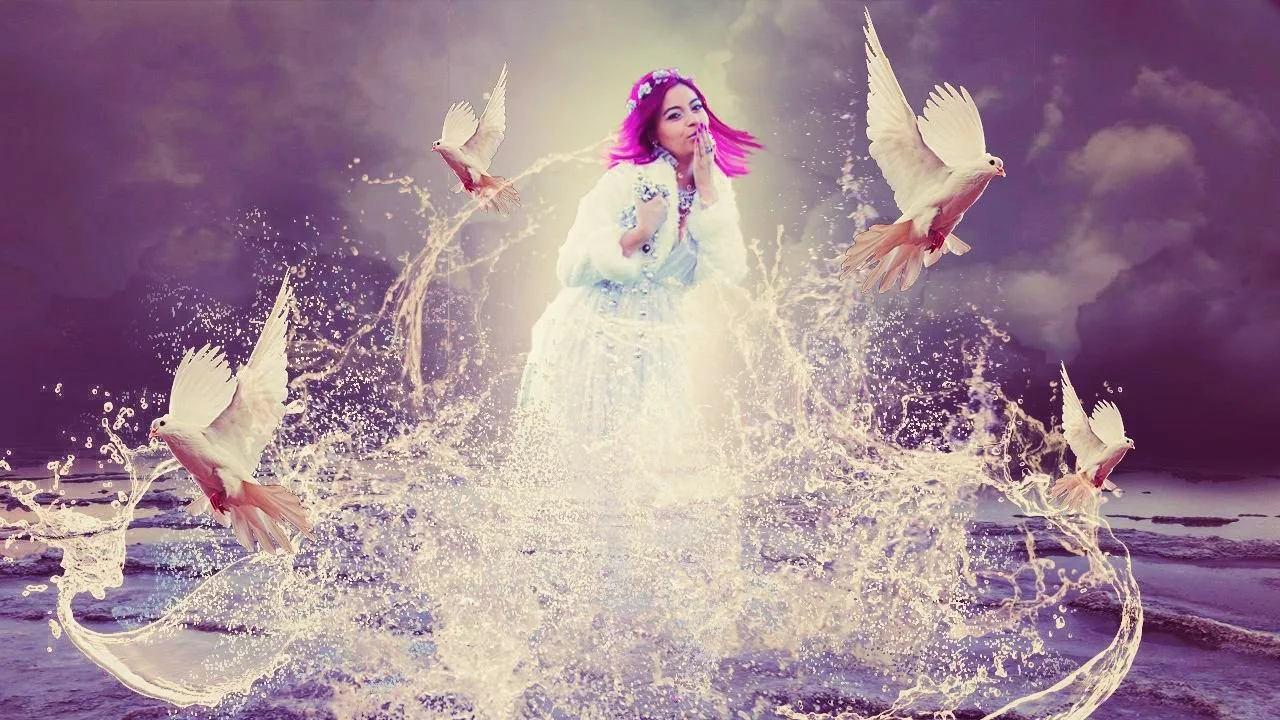A woman with pink hair, wearing a white dress, stands in water at the beach with a dark cloudy sky behind her. She is surrounded by five white doves flying around her, with splashes of water around her feet.
