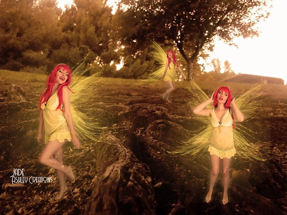 Image of three fairies with red hair and yellow dresses in a forest setting.