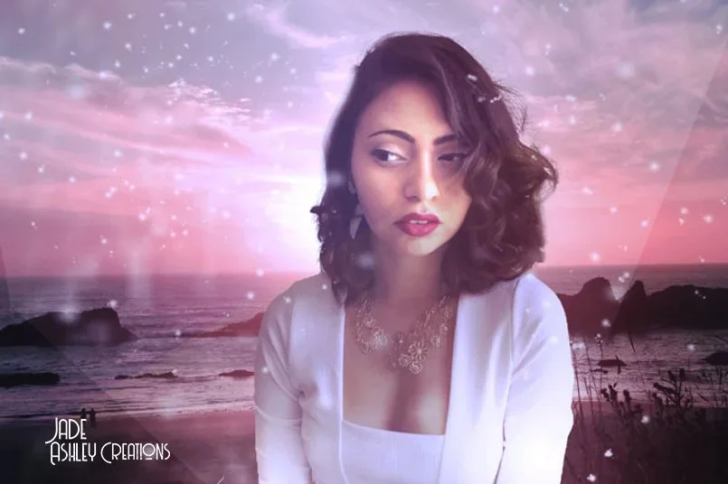 A woman with wavy brown hair and red lipstick poses against a digitally edited backdrop of a beach sunset with pink and purple hues, sparkles, and abstract light effects.