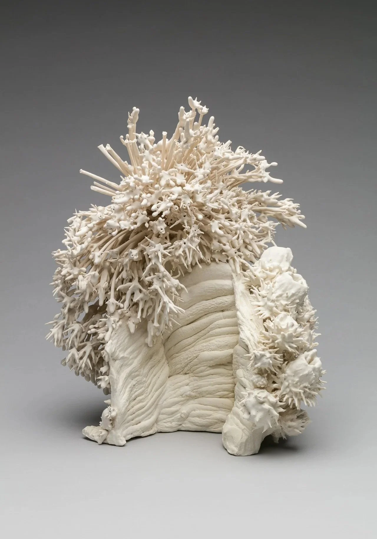 A modern, abstract ceramic vase with a textured turquoise surface and an irregular opening at the top, sitting on a light gray background.