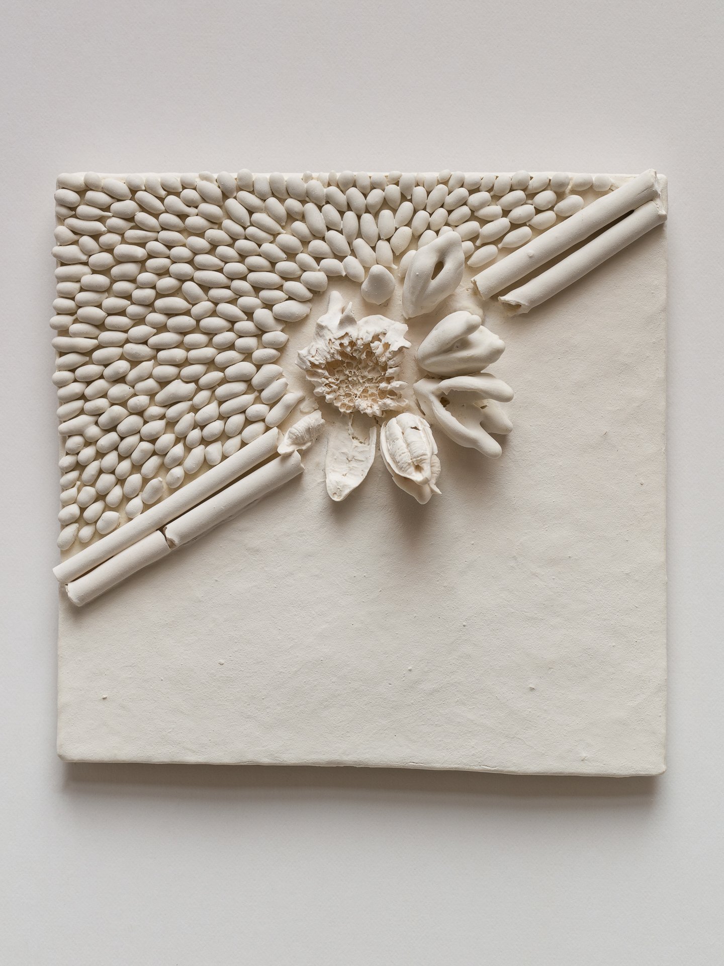A white textured square art piece with raised designs including a central flower, elongated petals, and two diagonal bamboo sticks, surrounded by small oval shapes.