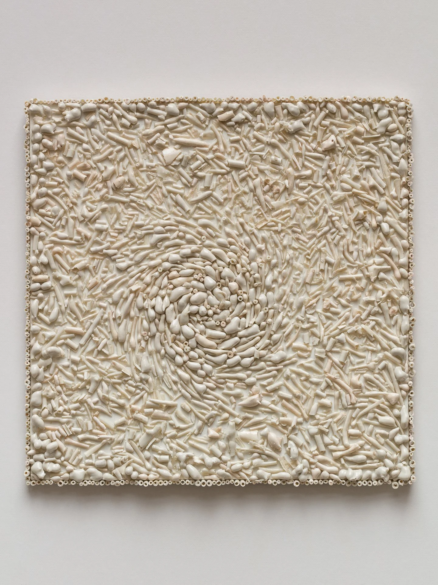 An abstract square art piece made of small white and off-white ceramic or plastic objects arranged in a swirling pattern.