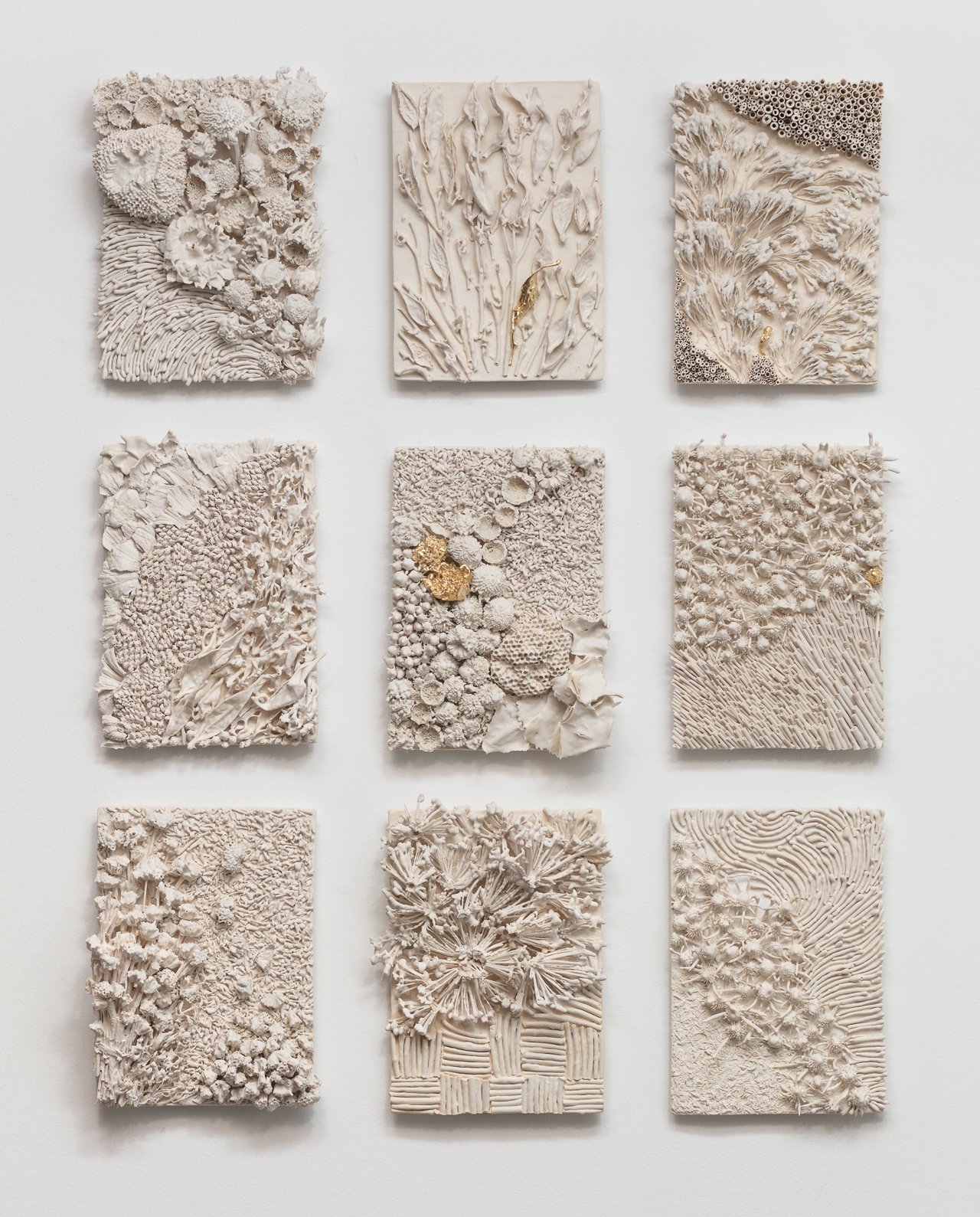 Nine square art panels with textured designs resembling natural elements like coral, leaves, and abstract patterns, displayed on a white wall.