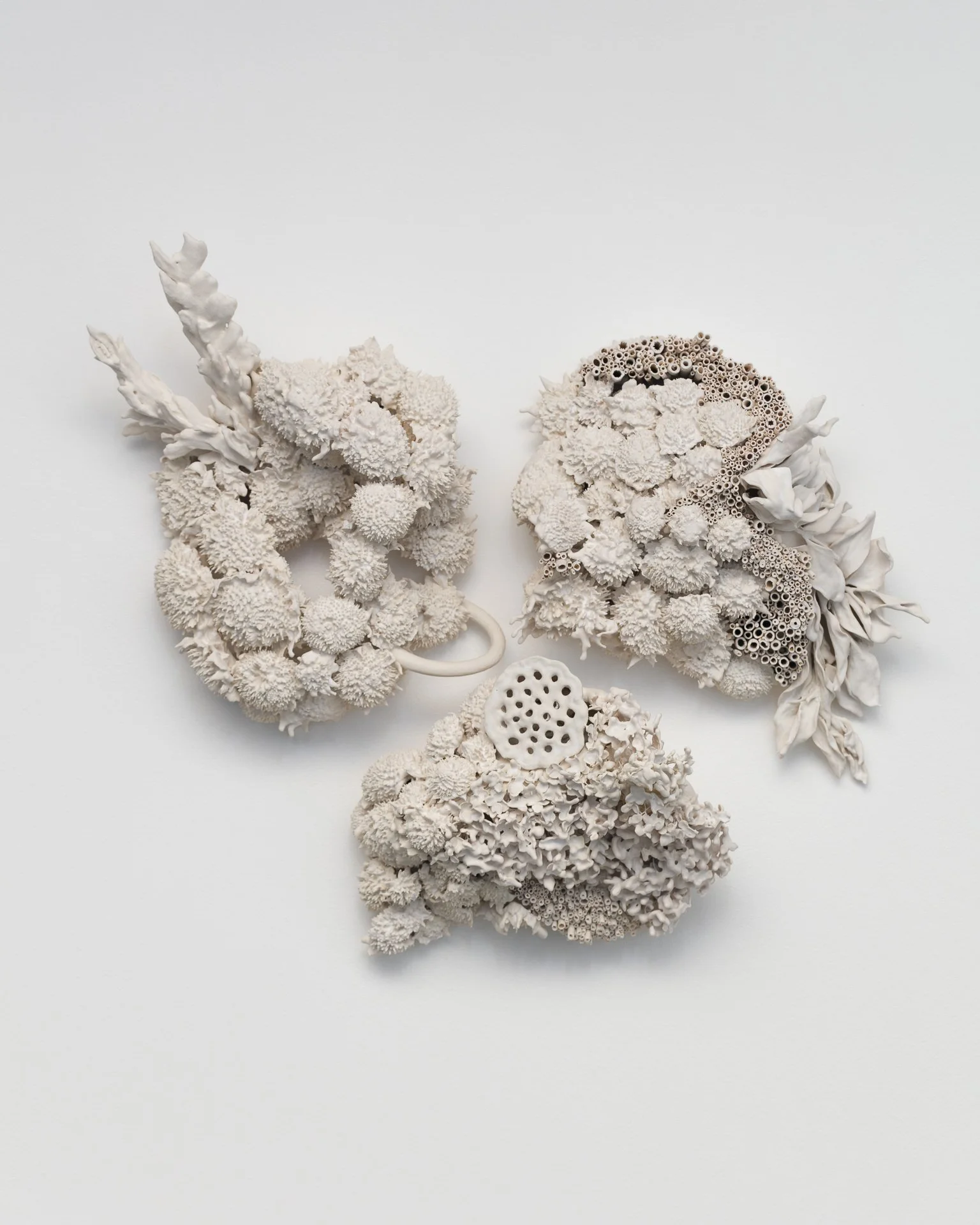 Three abstract sculptures made of white coral and ceramic, arranged on a white surface.