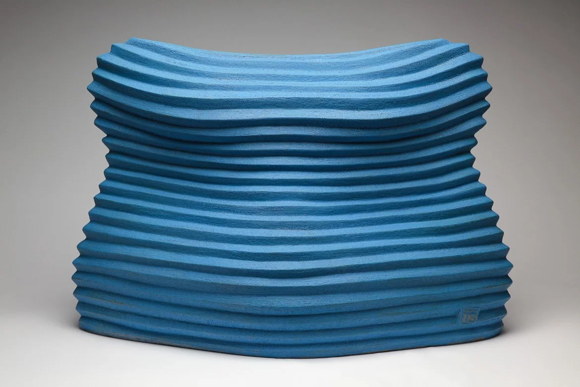 Blue textured modern ceramic sculpture of a headless bust with wavy horizontal lines, set against a plain background.