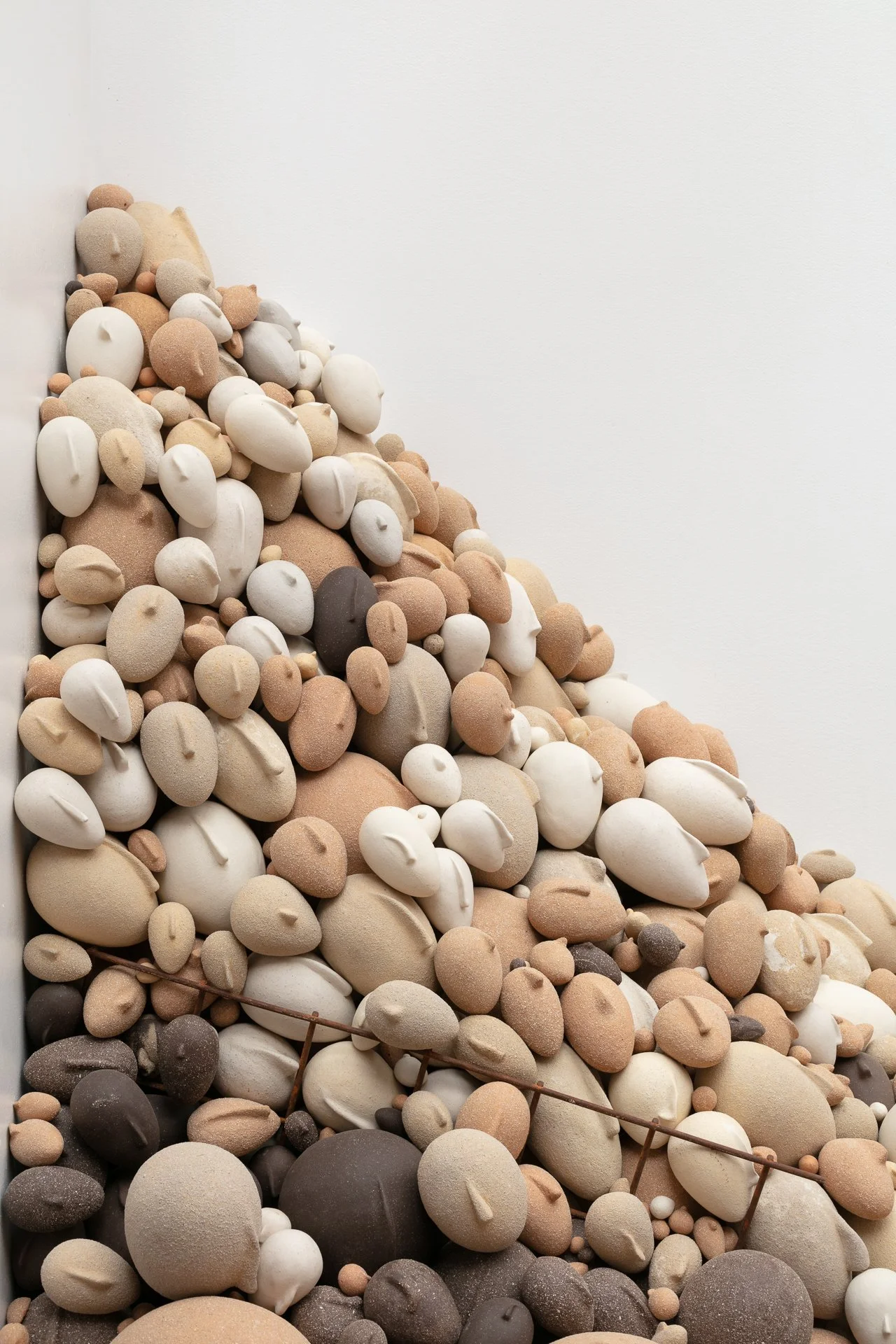 A wall art installation made of numerous beige, white, and dark brown pebble-like sculptures on a white wall.