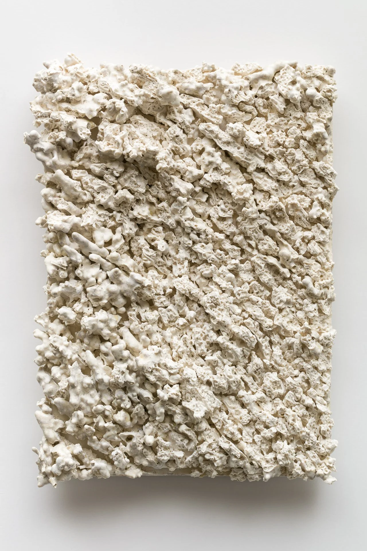 A textured white rectangular sculpture with rough, bumpy, and irregular surface made of what appears to be plaster or similar material, set against a plain background.