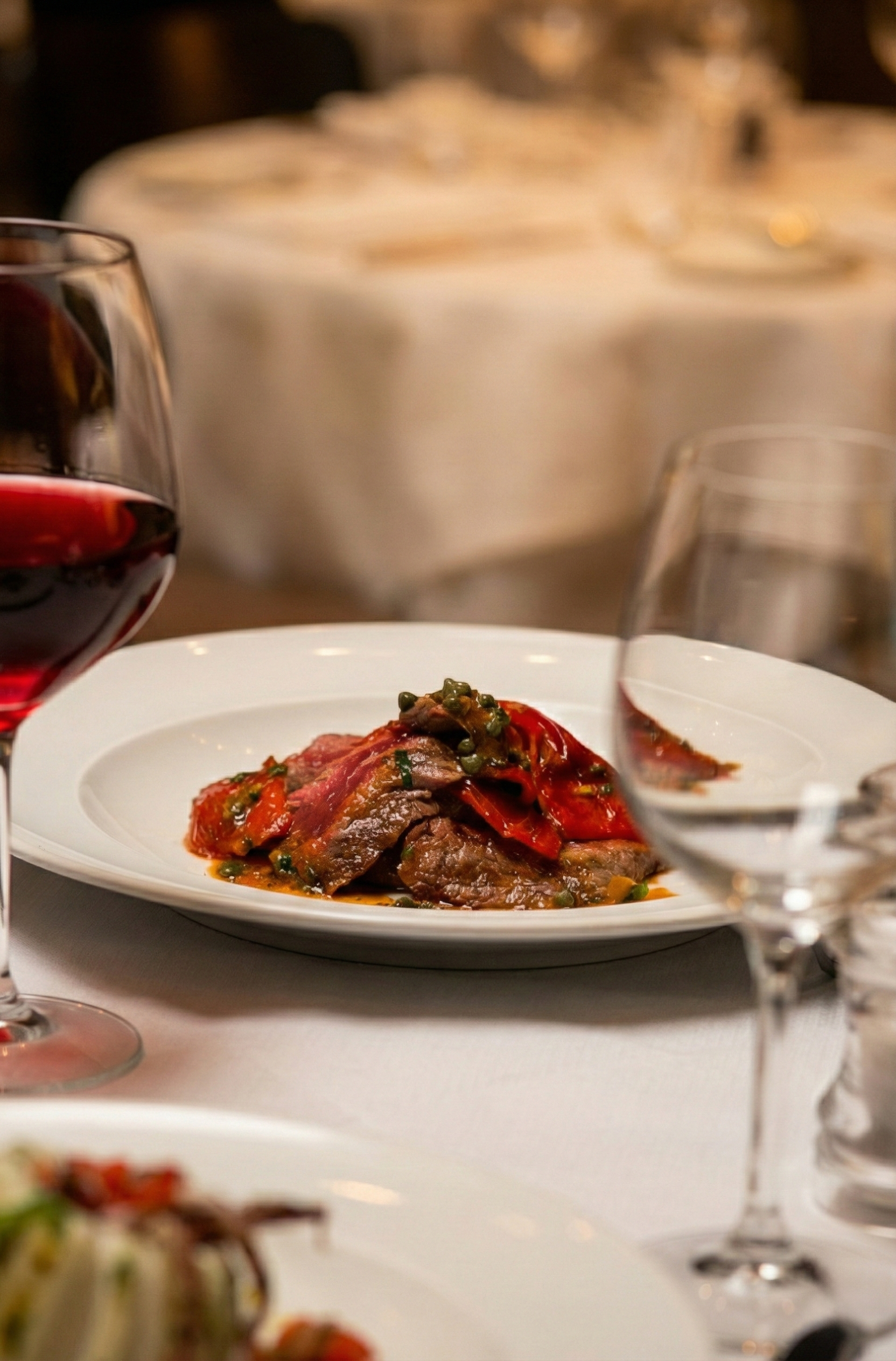 Plate of beef stew with vegetables on a dining table with glasses of red and white wine.