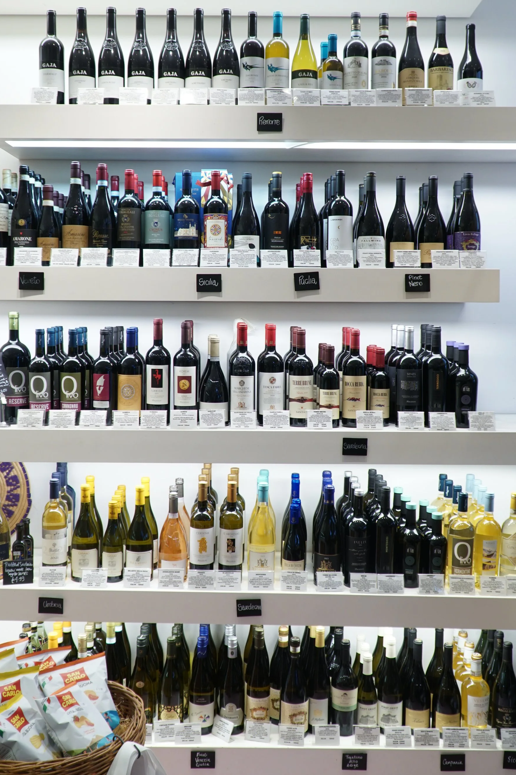 A shelf display of various bottles of wine organized by type and region, with signs indicating Italian, Sicilian, and other labels.