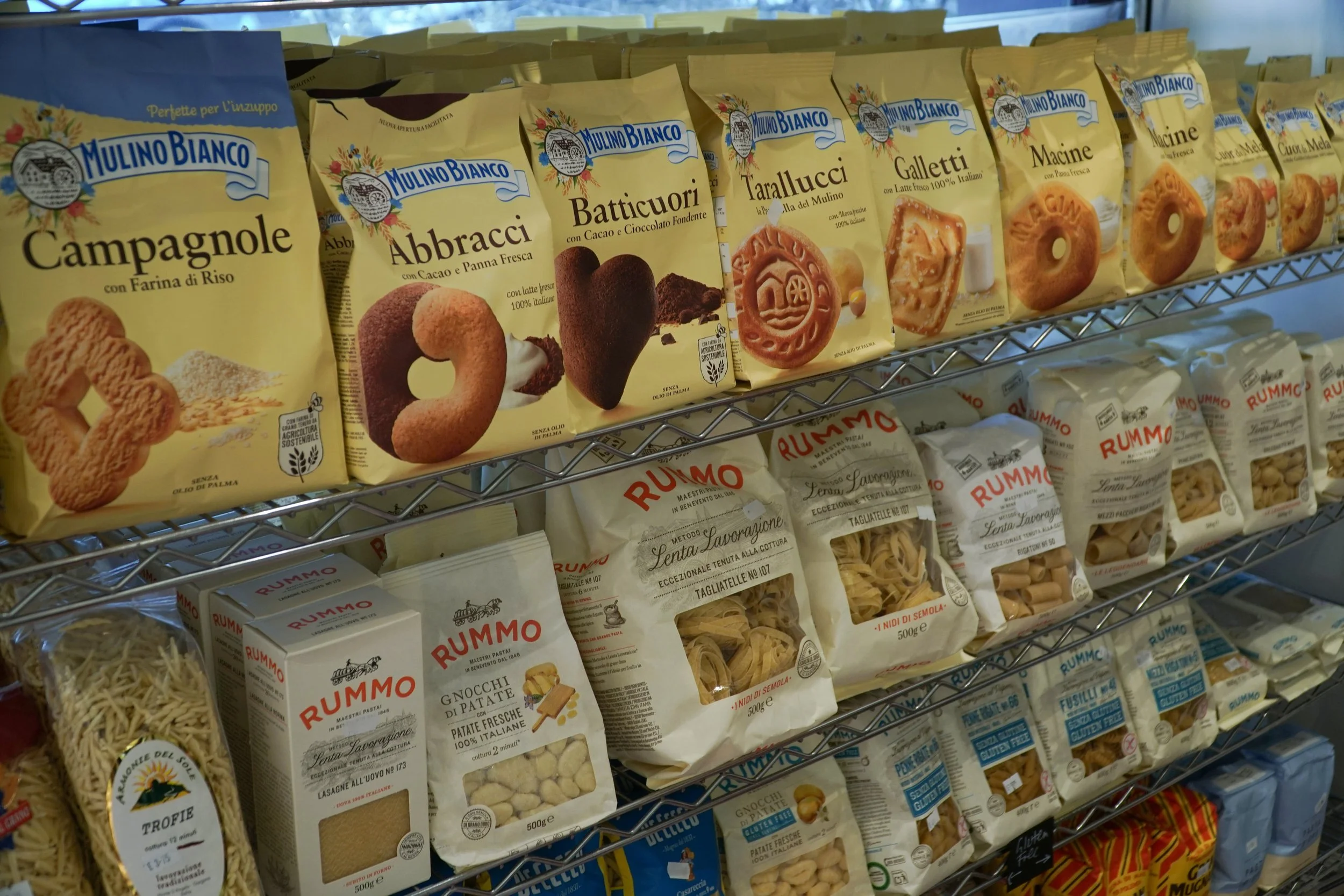 Shelves displaying various types of Italian pasta and cookies, including Mulino Bianco cookies and Rummo pasta packages.