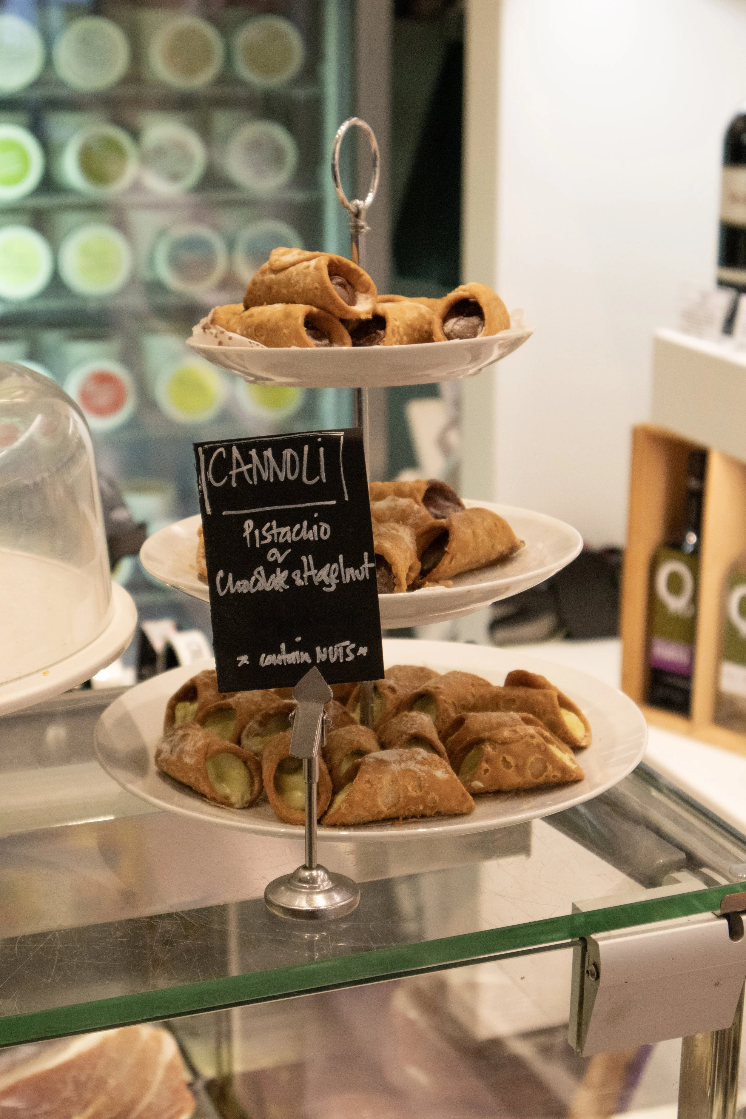 Plate of cannoli filled with pistachio, chocolate, and hazelnut; displayed on a three-tier stand inside a cafe.