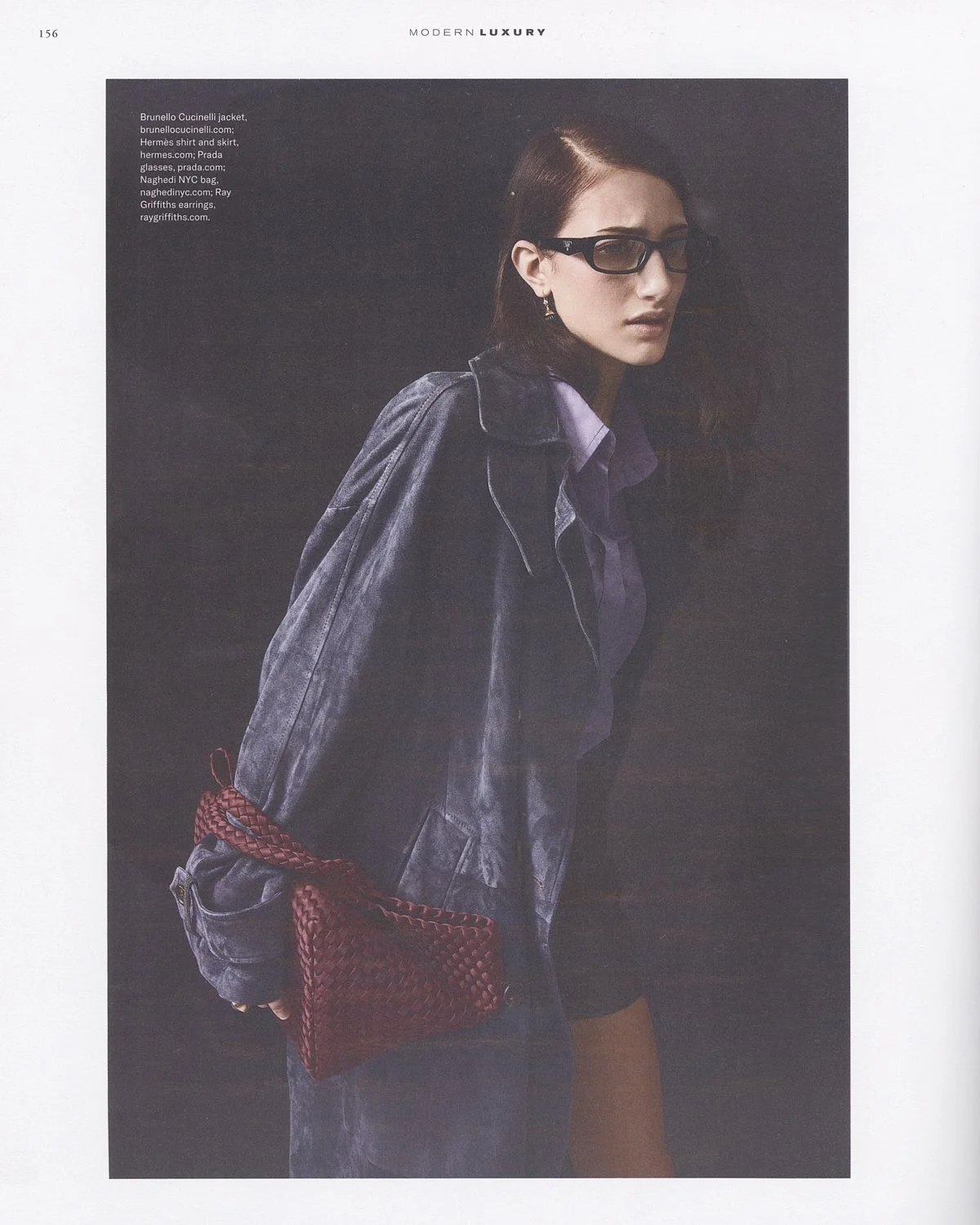 A woman wearing glasses, a dark denim jacket, and a purple shirt with a red woven handbag.