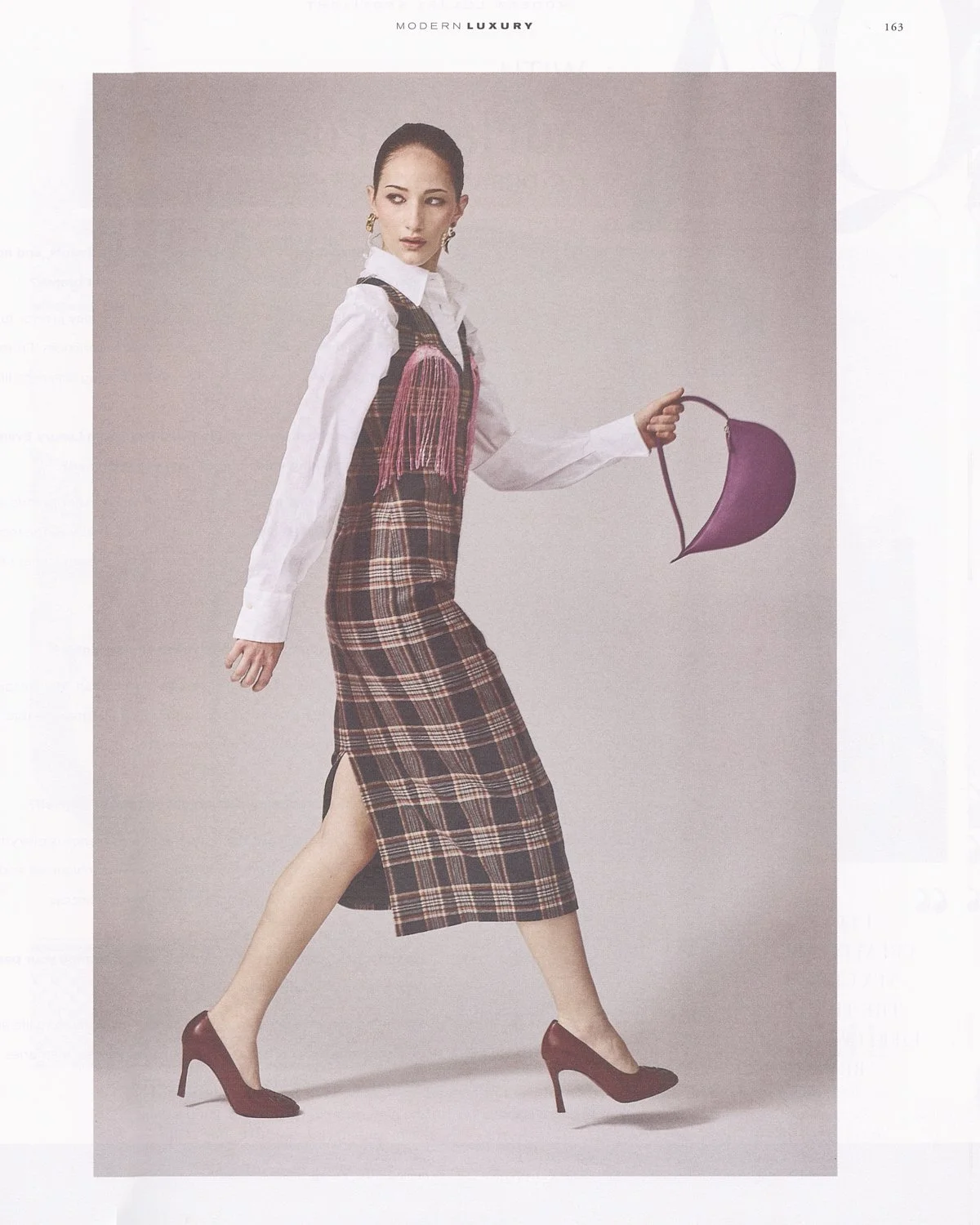 A woman in a plaid dress and high heels holding a purple purse, posing against a plain background.