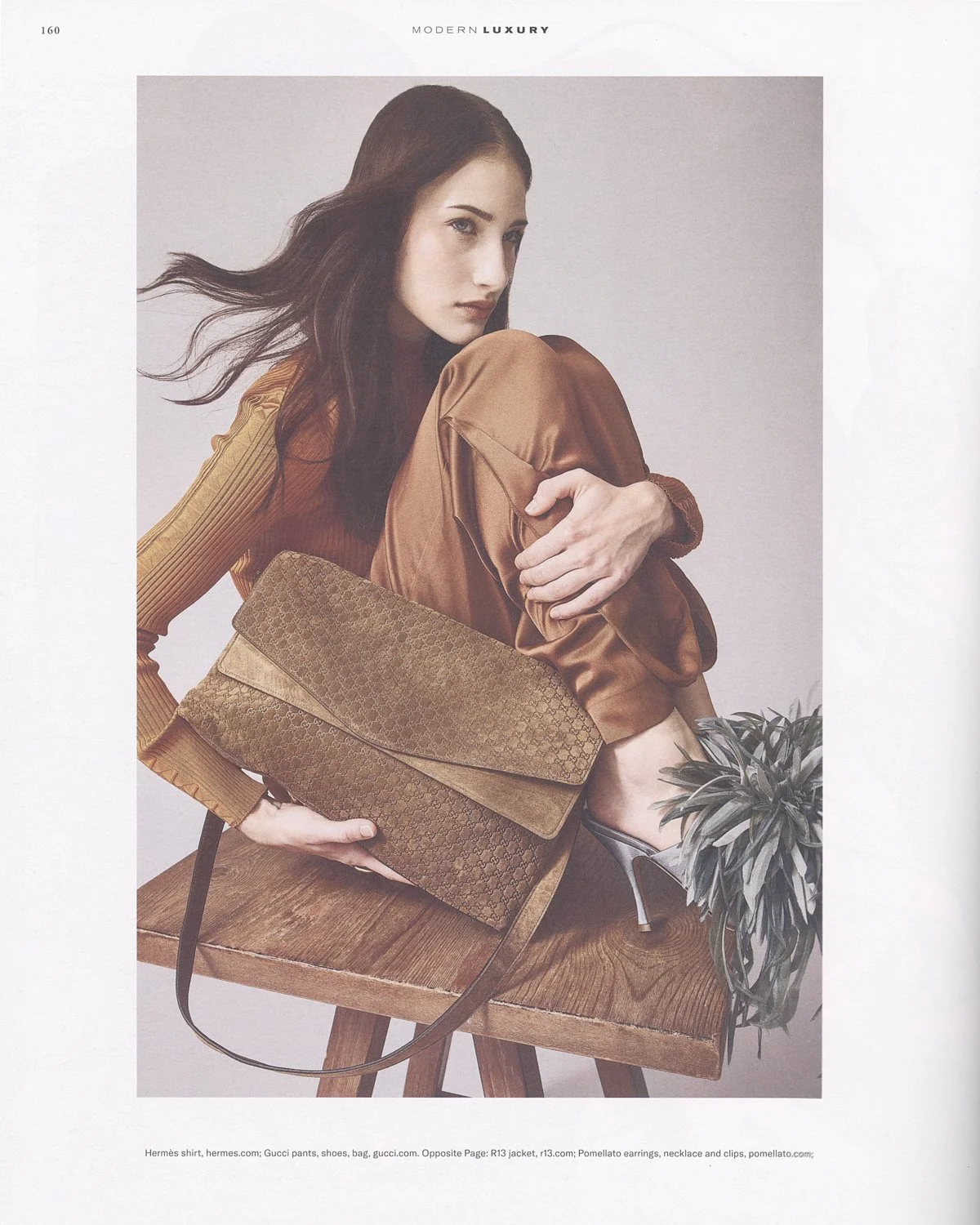 Fashion magazine photo of a woman with dark hair, wearing a brown satin jacket and Gucci pants, sitting on a wooden stool with a brown Gucci bag and a plant nearby.