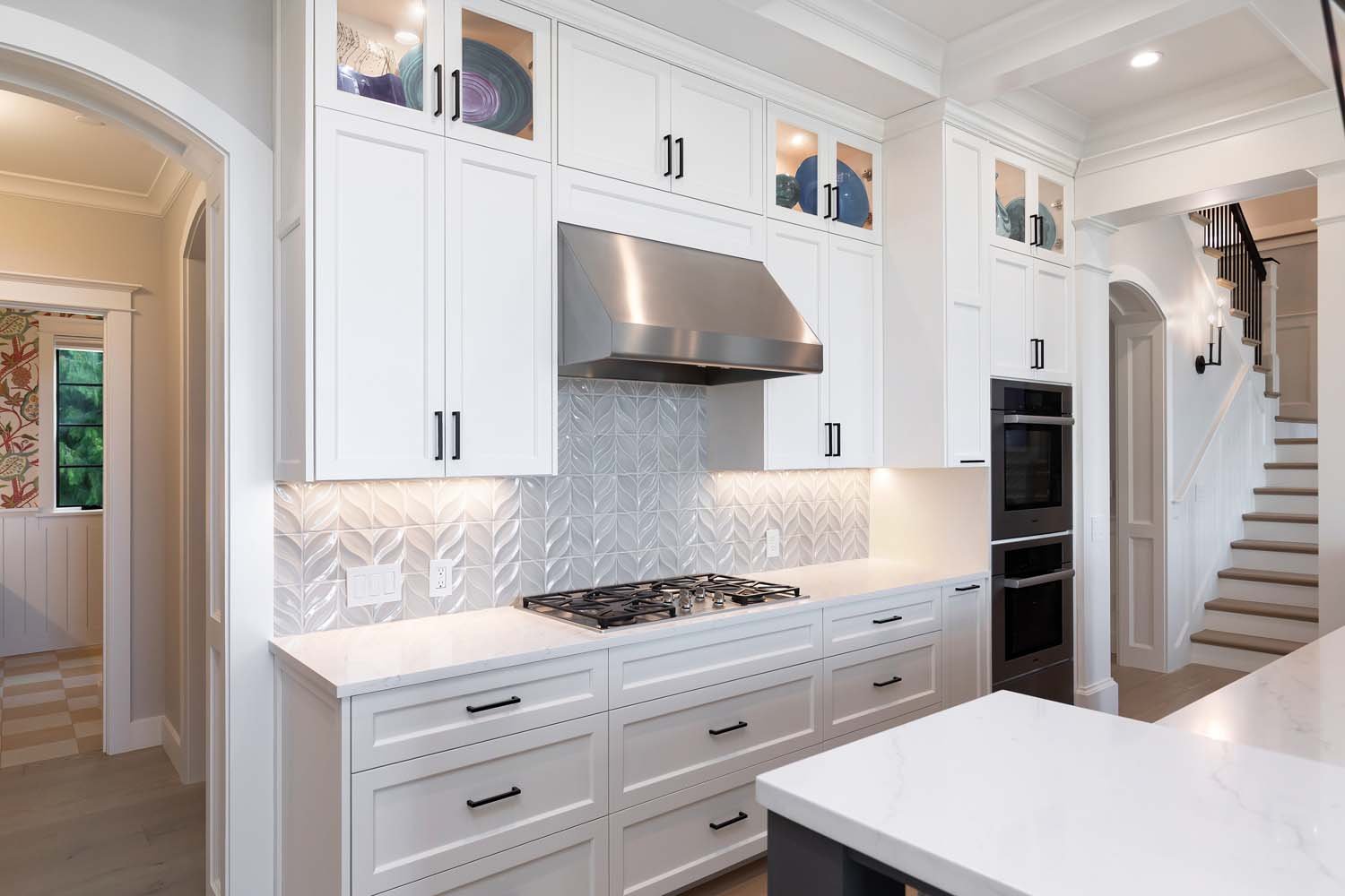 Elegant kitchen with white cabinetry, black handles, a stainless steel range hood, and backsplash tiles.