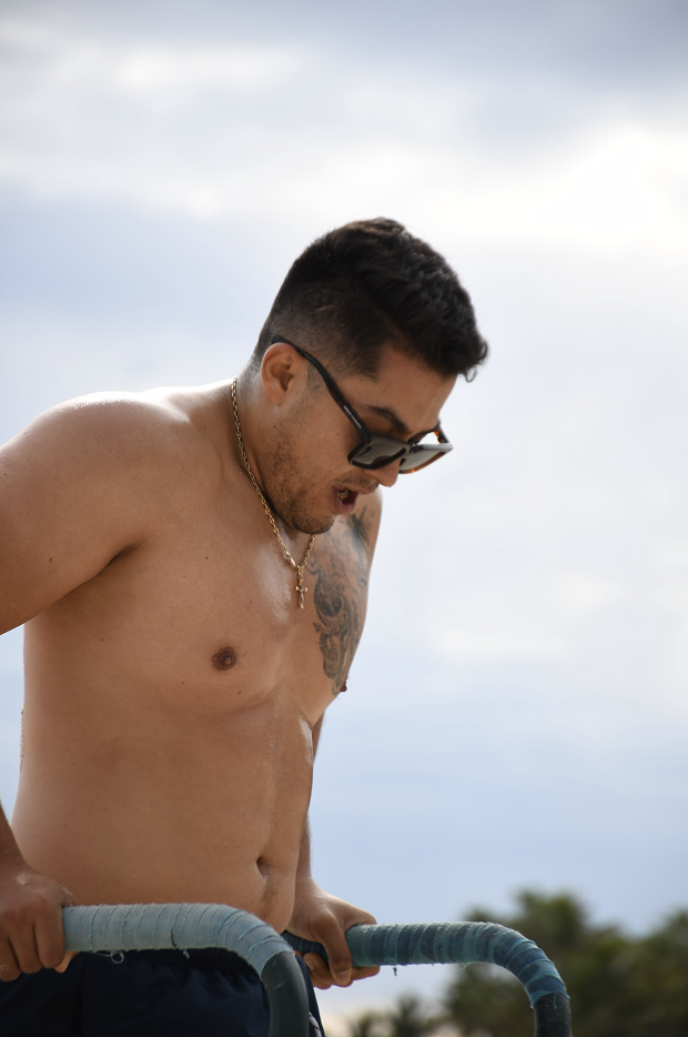 Joven sin camiseta con gafas de sol realizando ejercicio al aire libre.