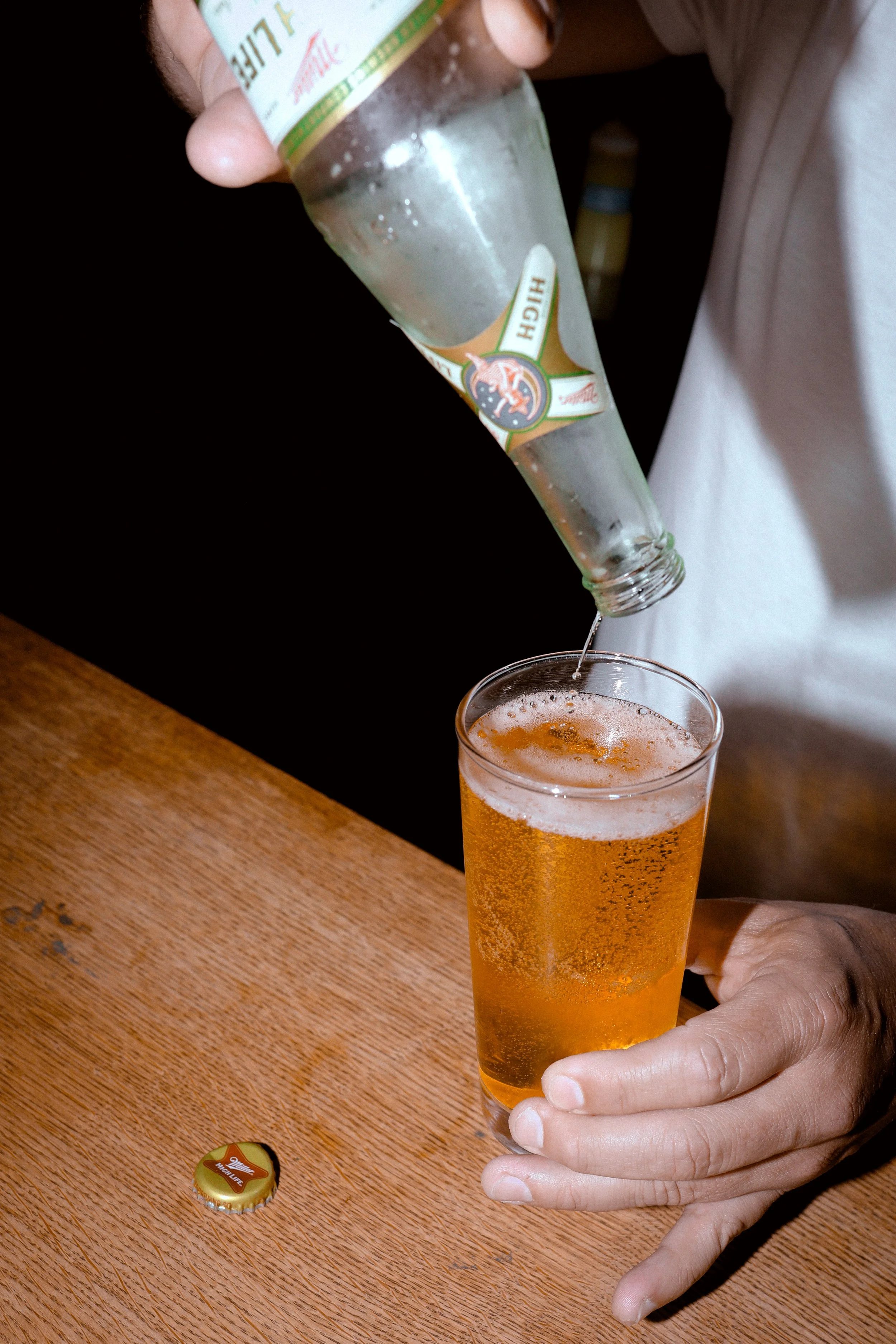 A person holding a tall glass of golden beer with bubbles, pouring more beer from a green, white, and red beer bottle.