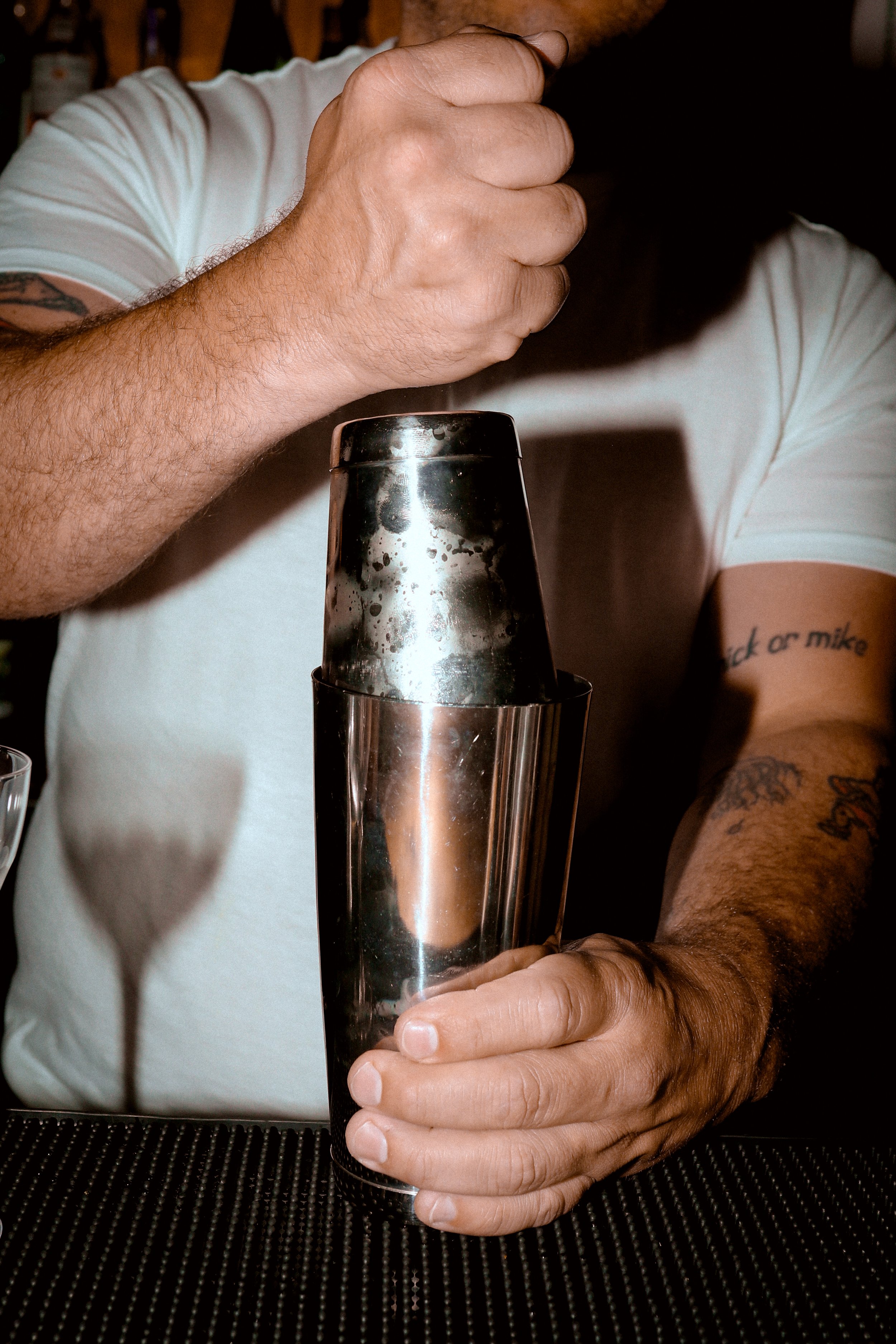 A person with tattooed arms using a cocktail shaker in a bar.