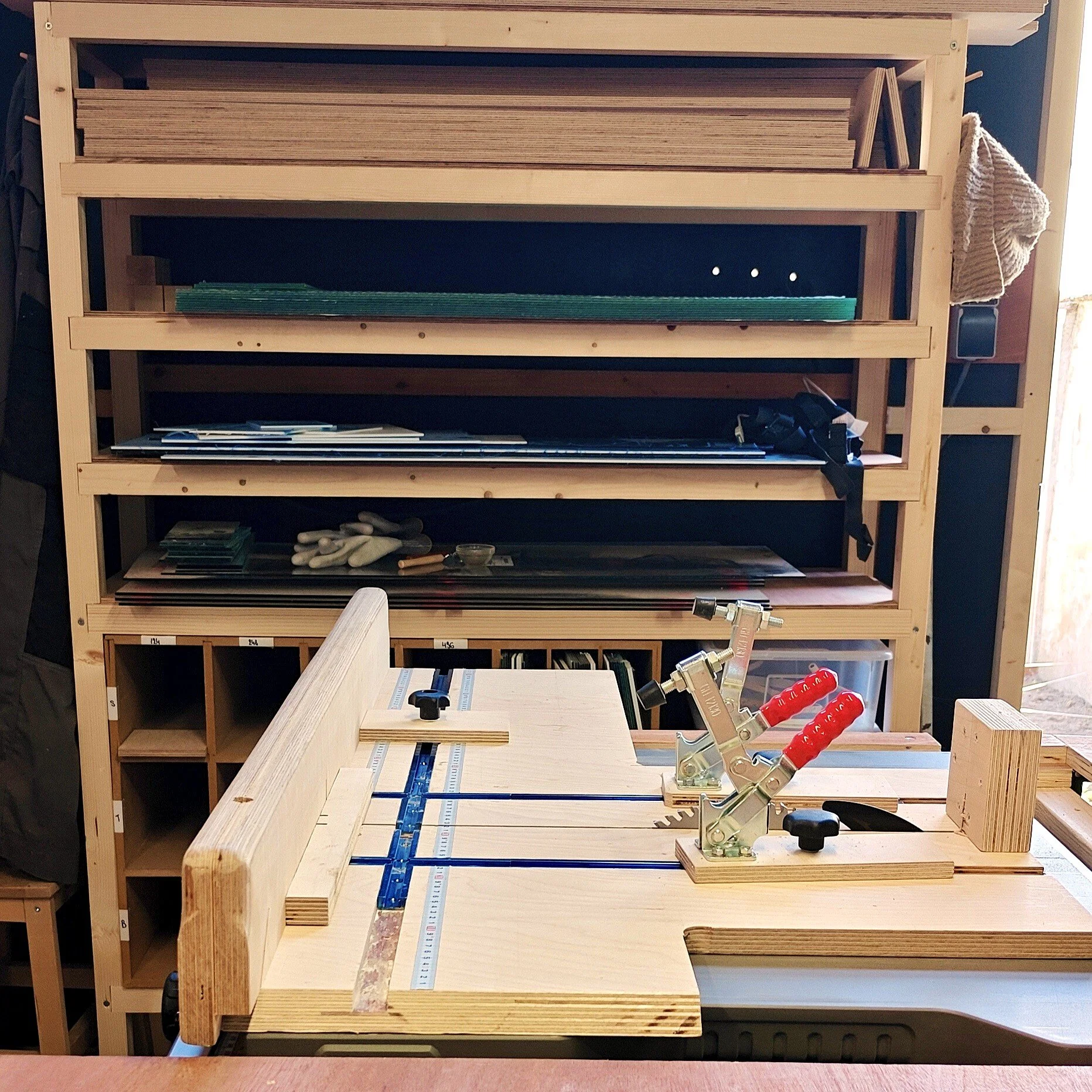 Wooden shelving unit with various woodworking tools, including clamps, rulers, and pieces of wood, in a woodworking shop.