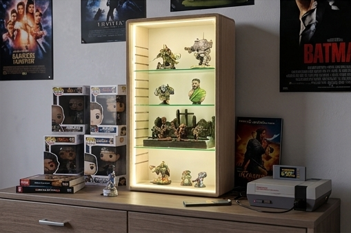 Display cabinet with illuminated glass shelves housing model figures, placed on a wooden surface near marquee and video game posters.