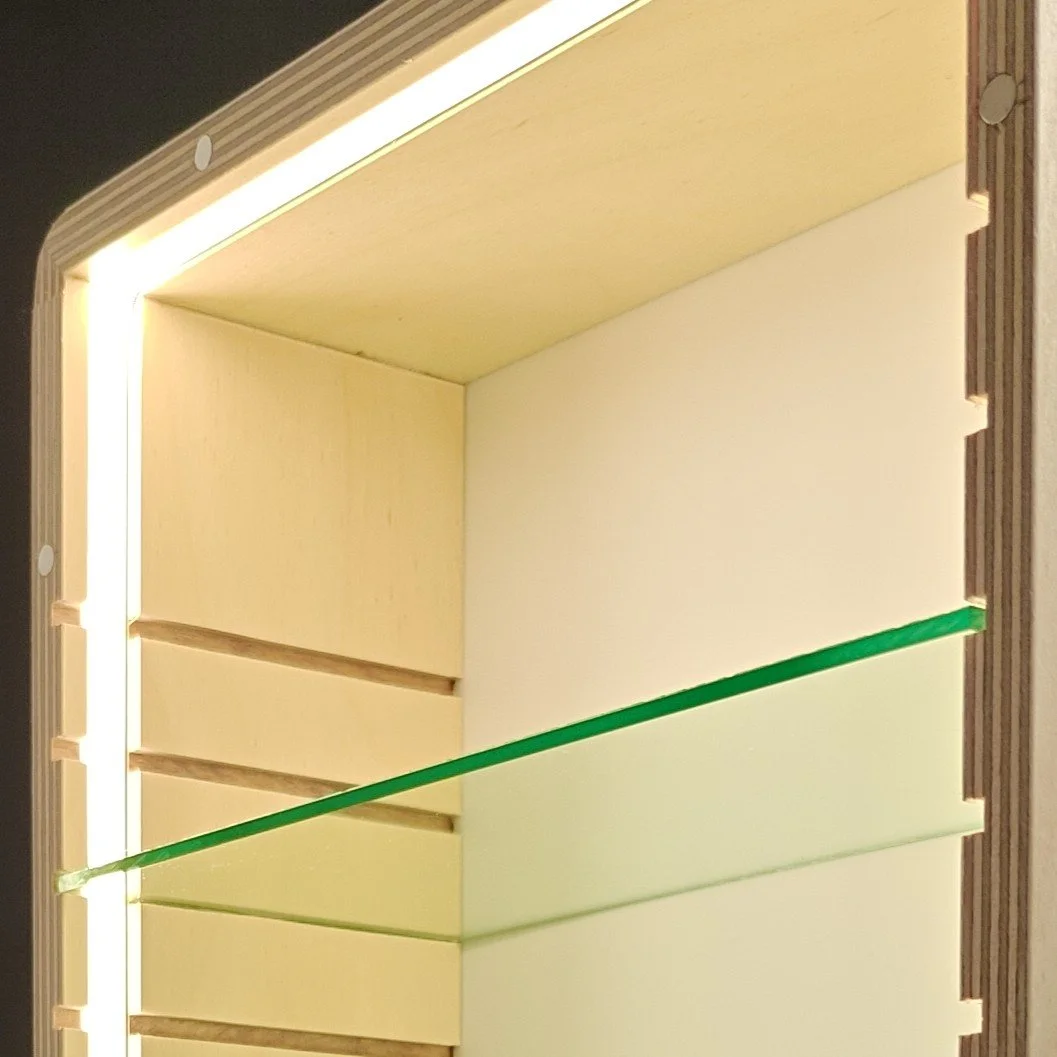 The inside of a wooden storage box with horizontal slots and a green glass rod running across the middle, illuminated from above.