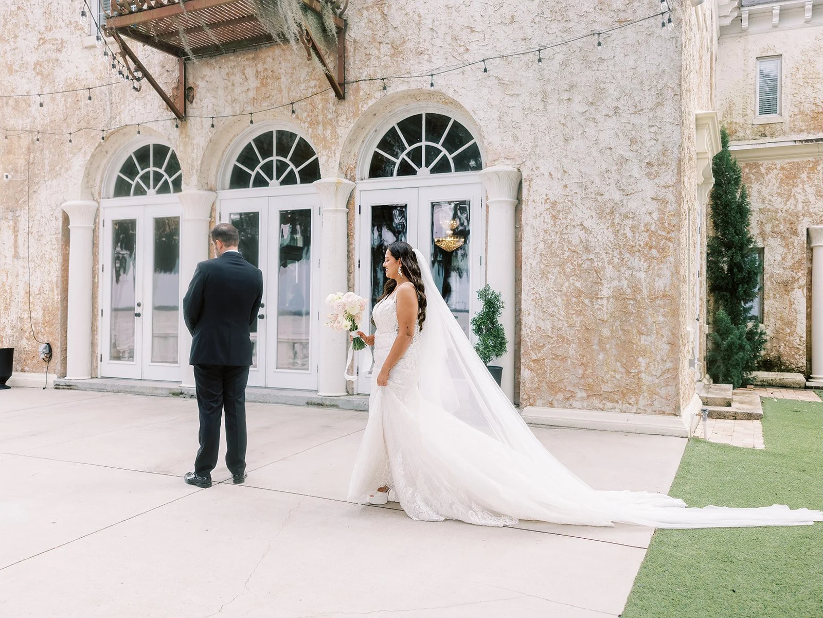 Side profile of bride walking on concrete path wearing a fitted lace dress with bouquet.