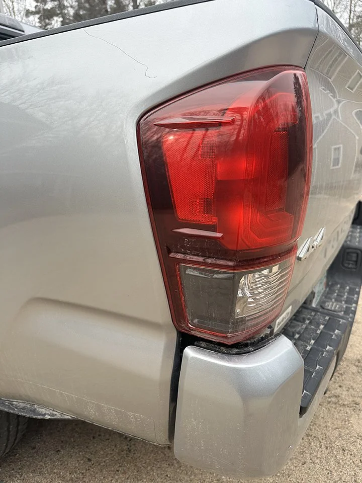 Close-up of the rear right corner of a silver pickup truck, showing the tail light and bumper.