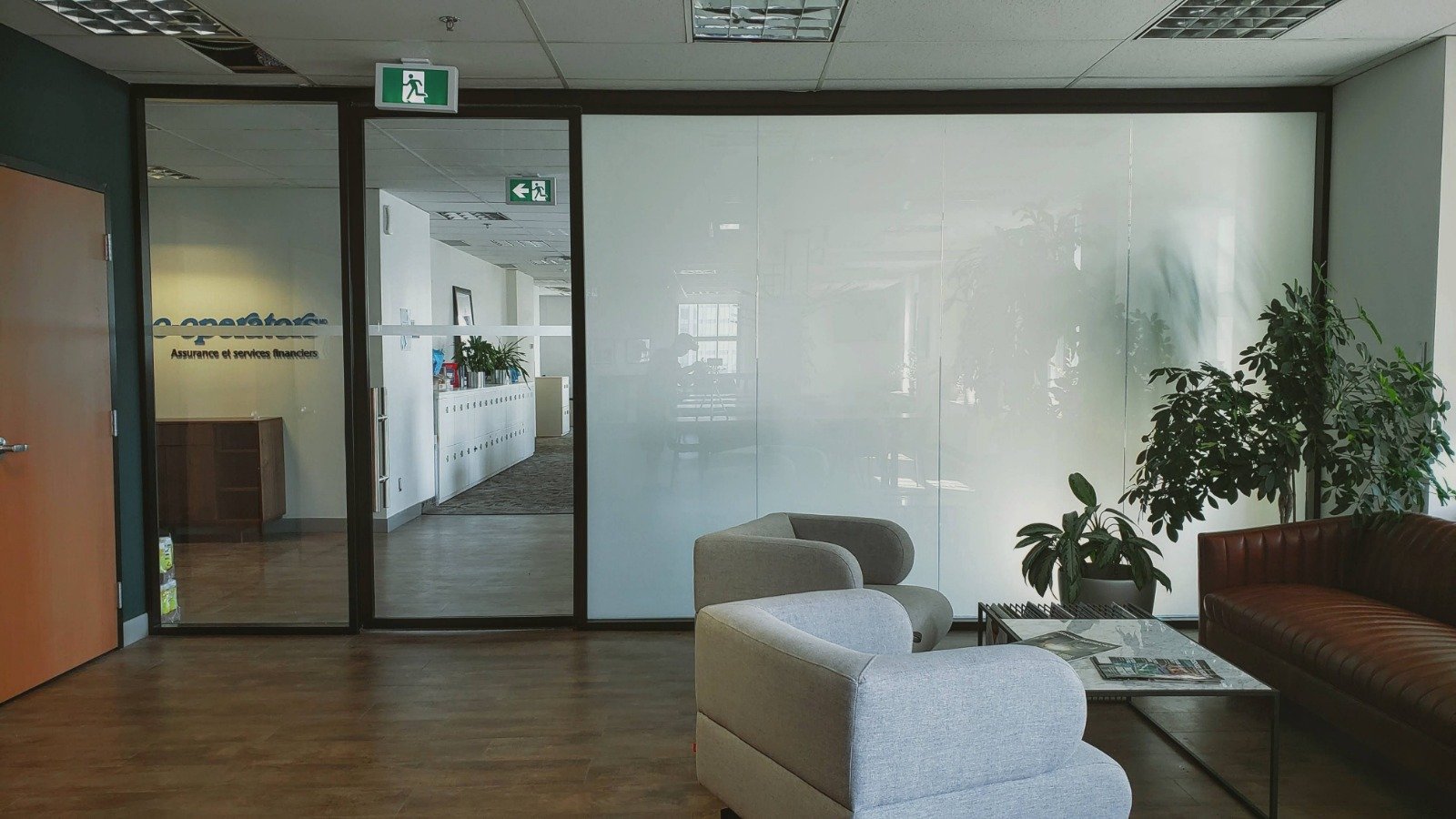 Office waiting area with couches, plants, and a hallway with lockers and office signs.