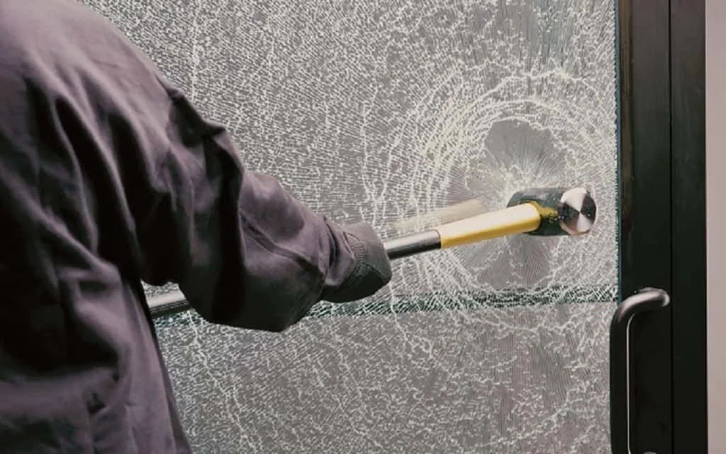 Person using a hammer to break a glass door