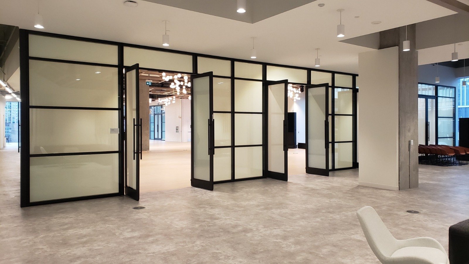 Modern interior space with glass partition doors, white walls, pendant lighting, and a white chair in the foreground.