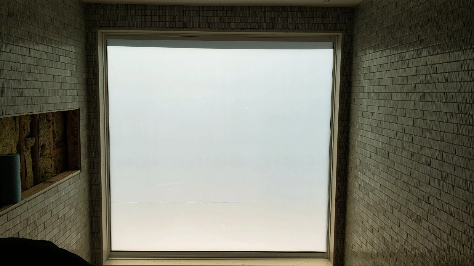 View of a frosted glass window in a brick wall with an opening for a light fixture or vent on the left side.