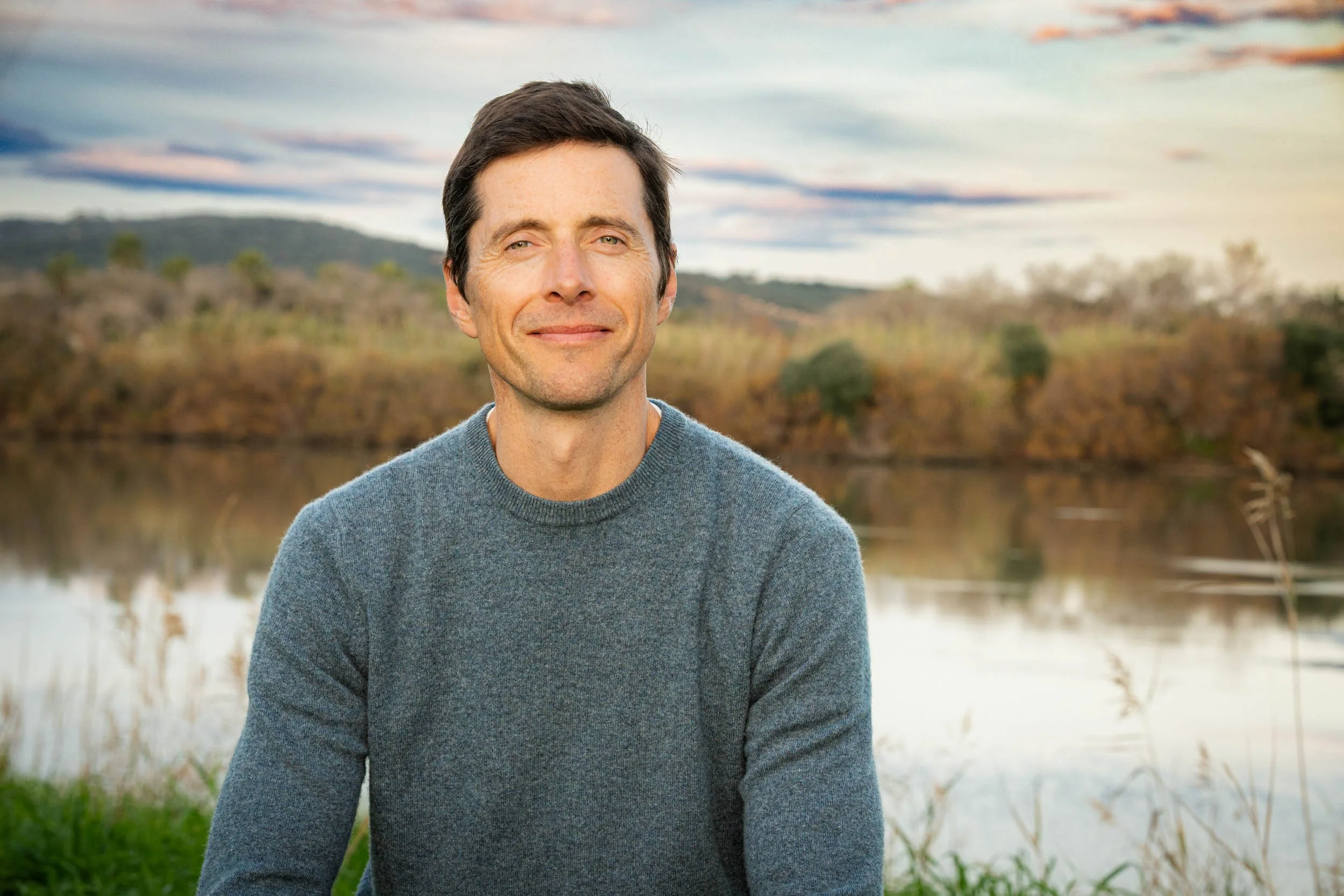 Andrew Scriven smiling in front of river at sunset