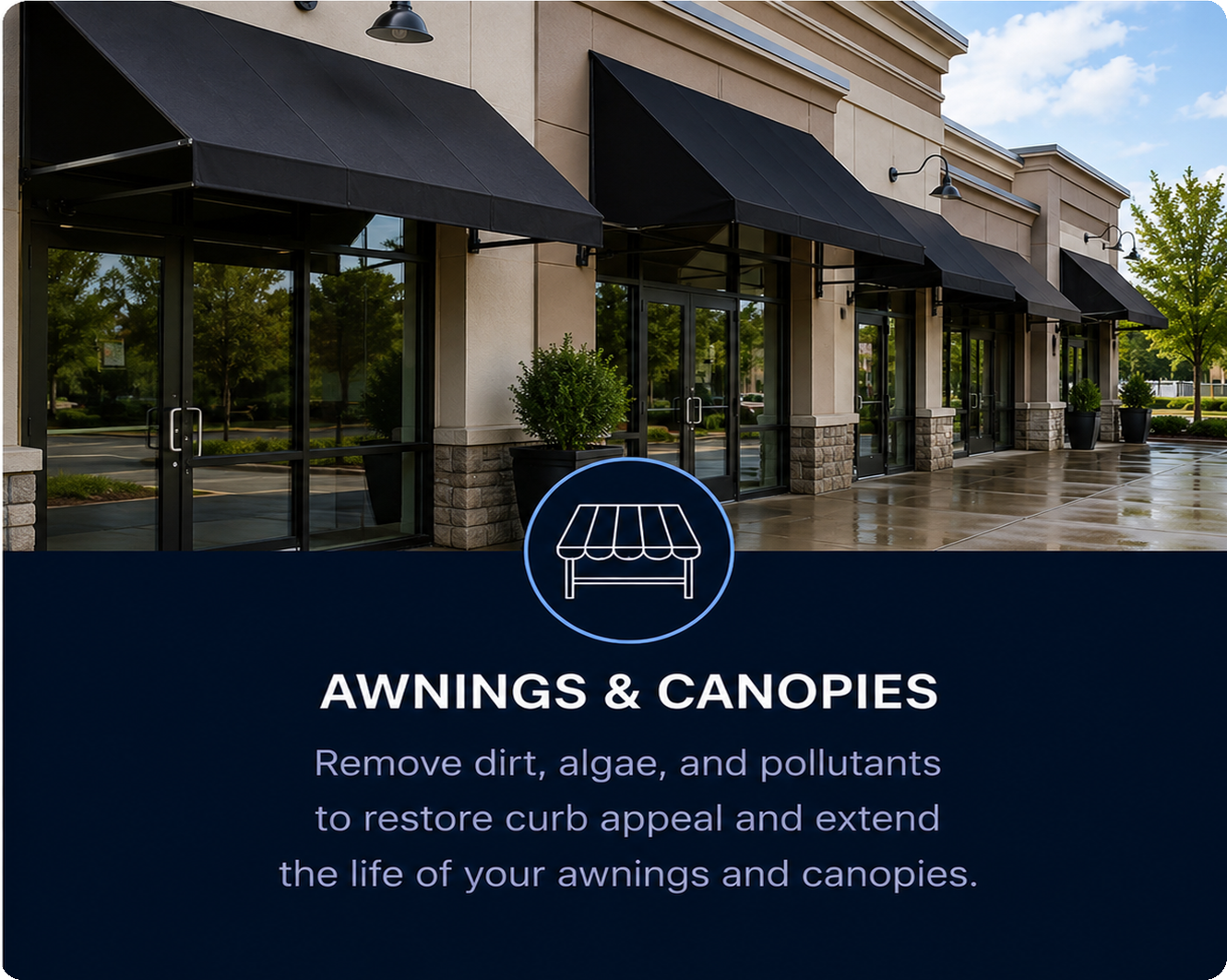A shopping plaza with multiple storefronts featuring black awnings, large glass doors, and potted plants in front. The sky is partly cloudy and the wet pavement suggests recent rain.