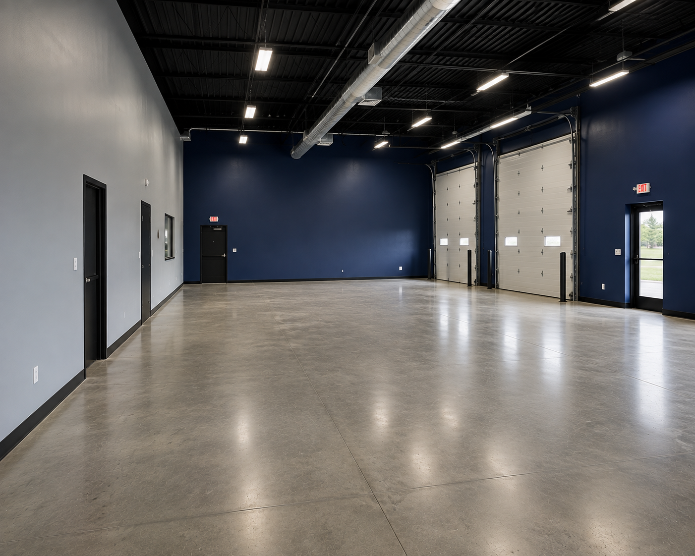 Empty industrial warehouse or garage with polished concrete floor, blue and gray walls, high ceiling, and large garage doors.
