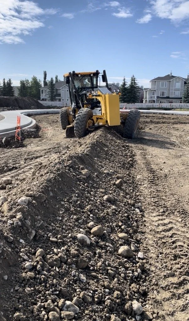 A yellow bulldozer moving dirt and rocks at a construction site, with residential houses and a blue sky in the background.