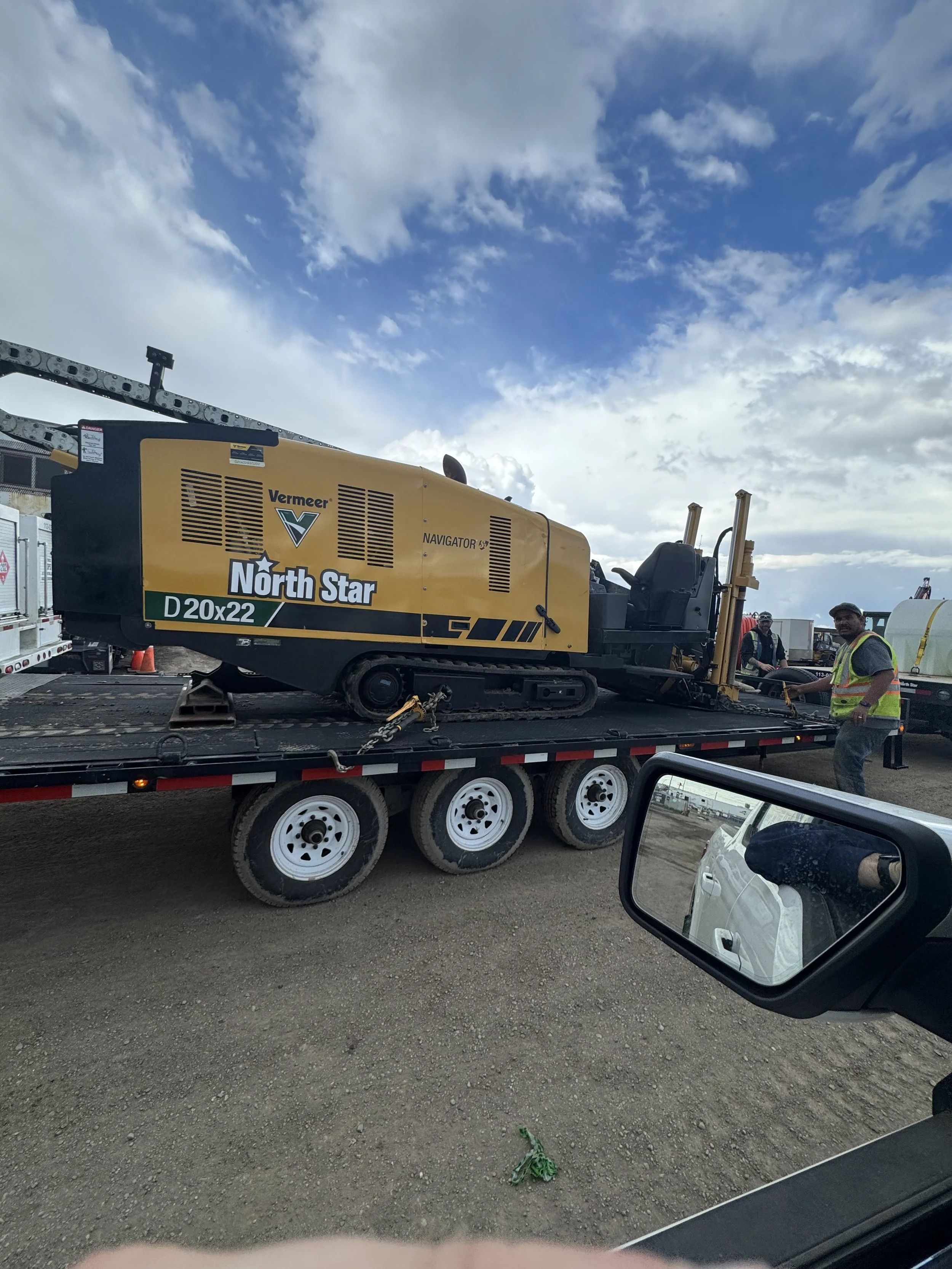 A large construction or road maintenance machine labeled 'North Star' on a flatbed truck, with workers standing nearby, under a partly cloudy sky.