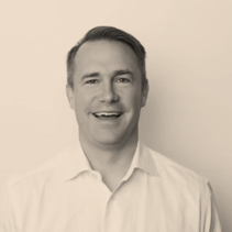 Portrait of a smiling man with short hair, wearing a collared shirt, against a plain light background.
