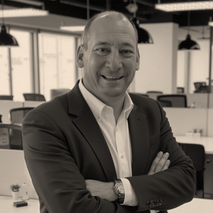 A man in a suit smiling with his arms crossed in an office environment.