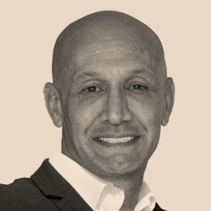 Black and white portrait of a smiling man with a bald head, wearing a collared shirt and blazer.